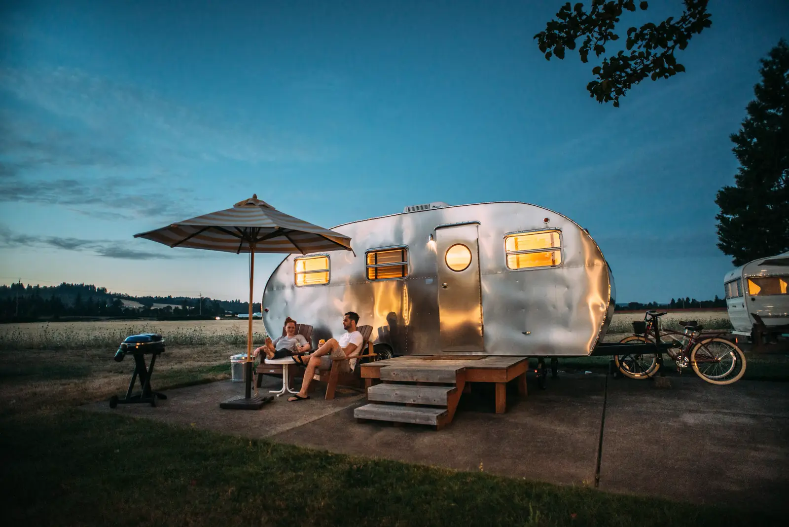 A couple relaxing outside their camper at dusk