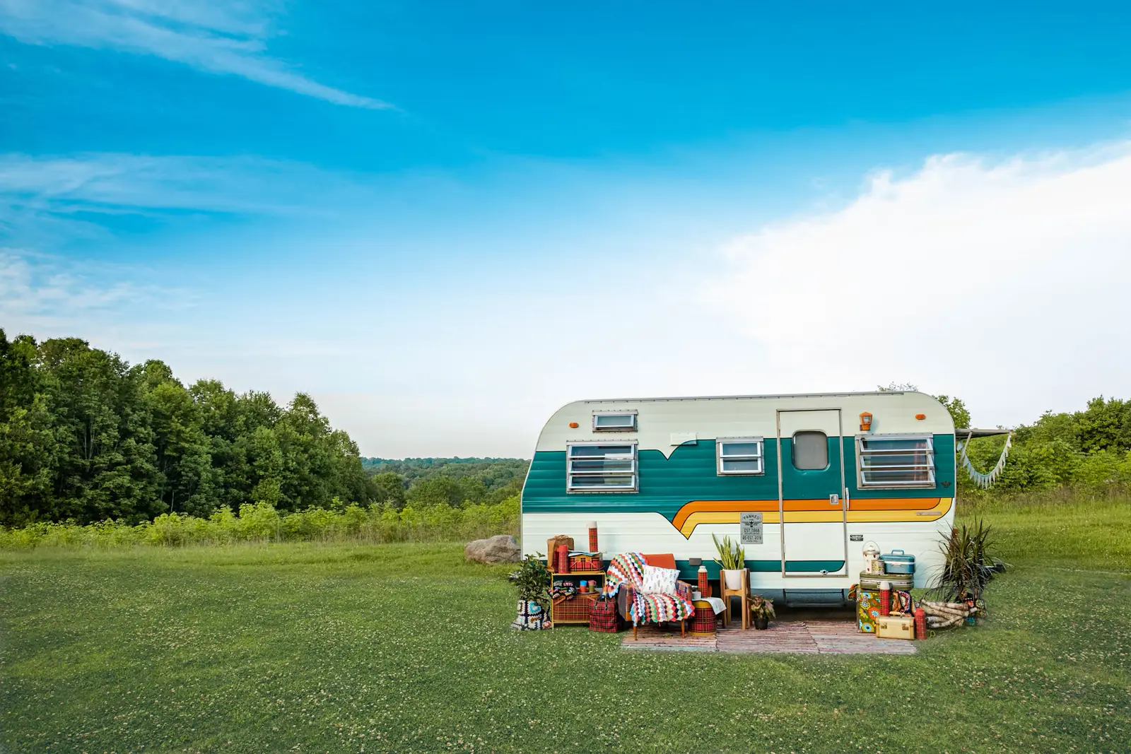 Vintage camper parked in a green field under a blue sky