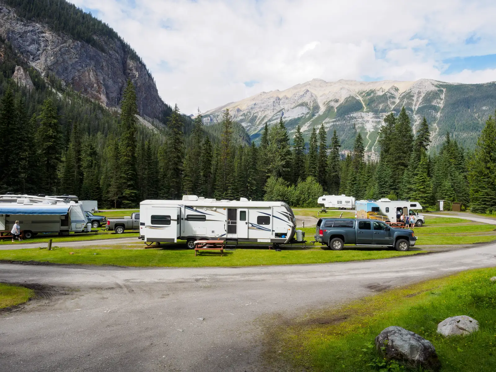 Travel trailers and trucks at a campground below snow-capped mountains