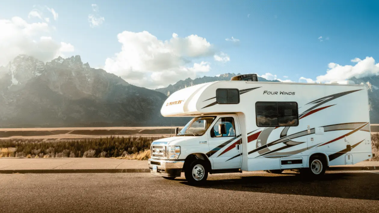 A Class C motorhome on a road below mountain peaks