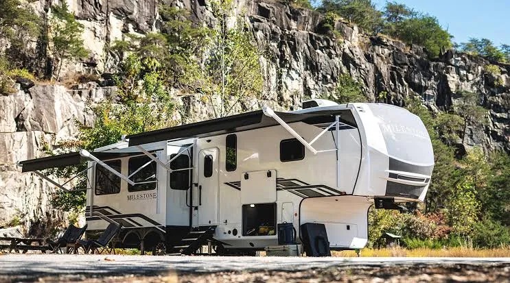 A fifth wheel RV with its awnings out in front of a rocky cliff
