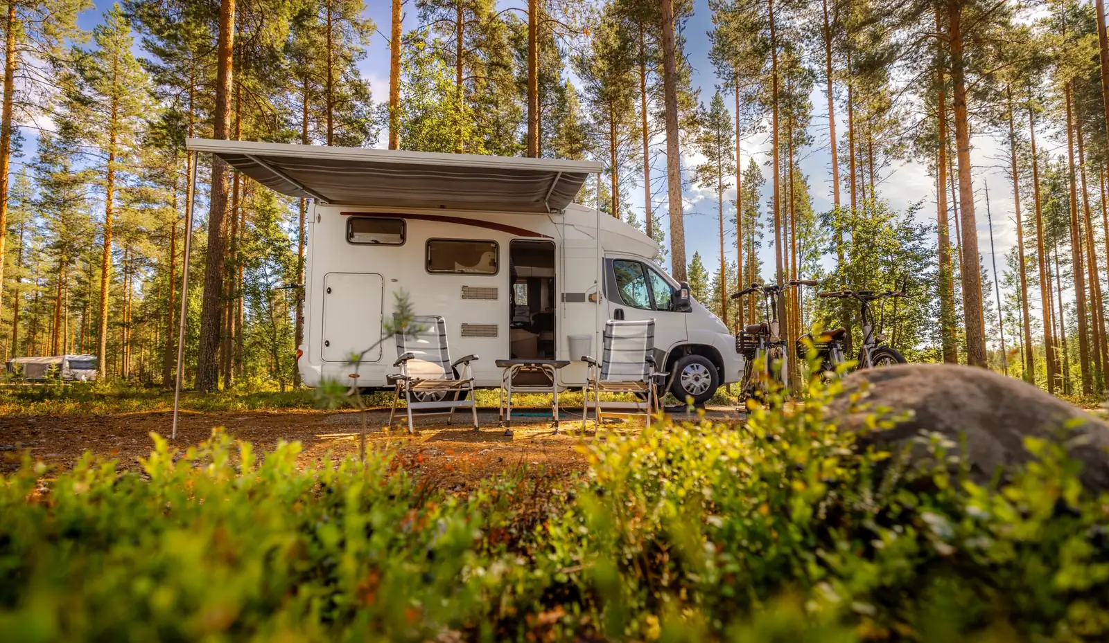 A motorhome with its awning out at a sunny forest campsite