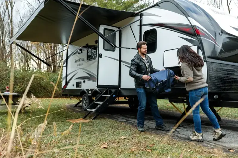 A couple loading a bag into their travel trailer at a campsite